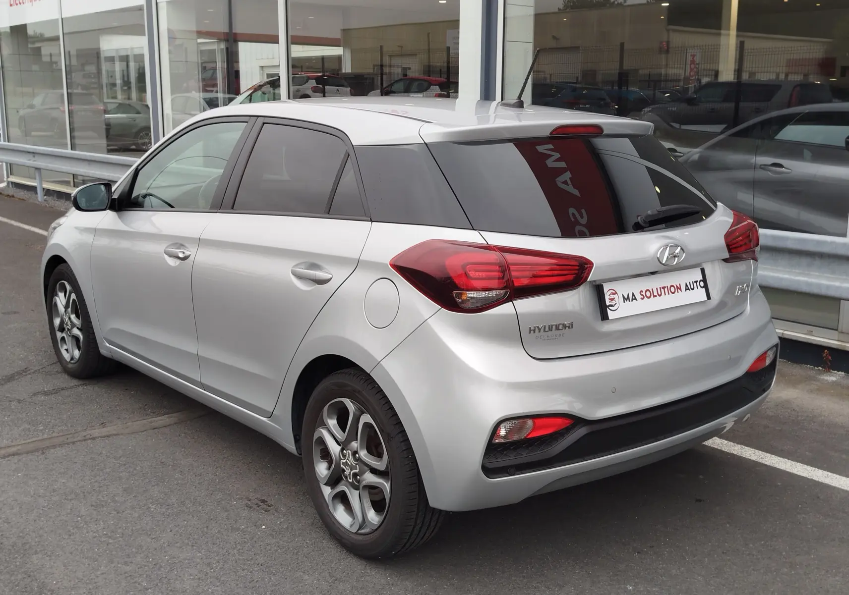 Vue 3/4 arrière droite d'une Hyundai i20 2018 gris argenté avec vitres teintées et feux arrière LED visibles.
