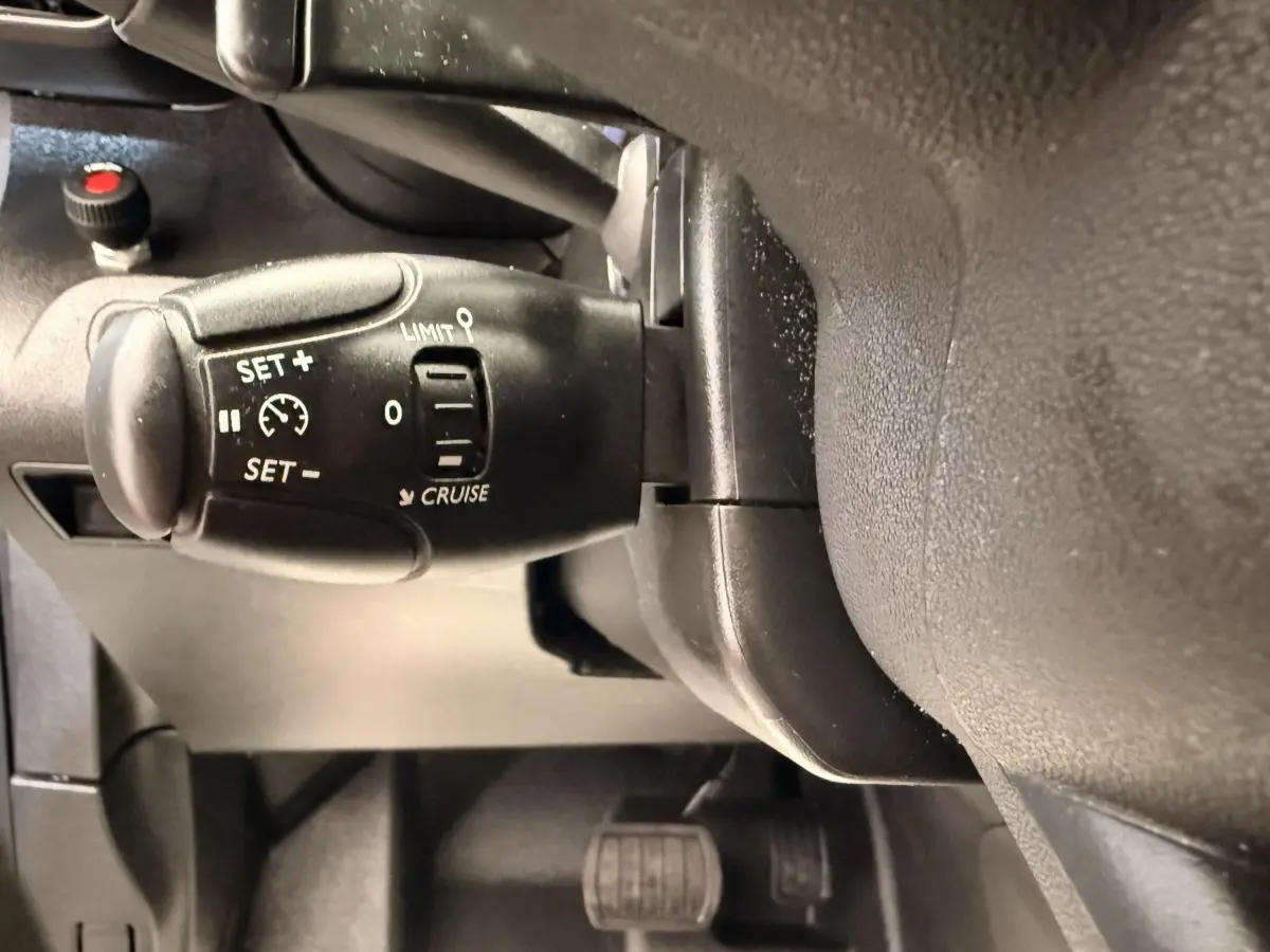 Gros plan sur la commande de régulateur de vitesse à gauche du volant dans l'habitacle du Citroën Berlingo blanc.