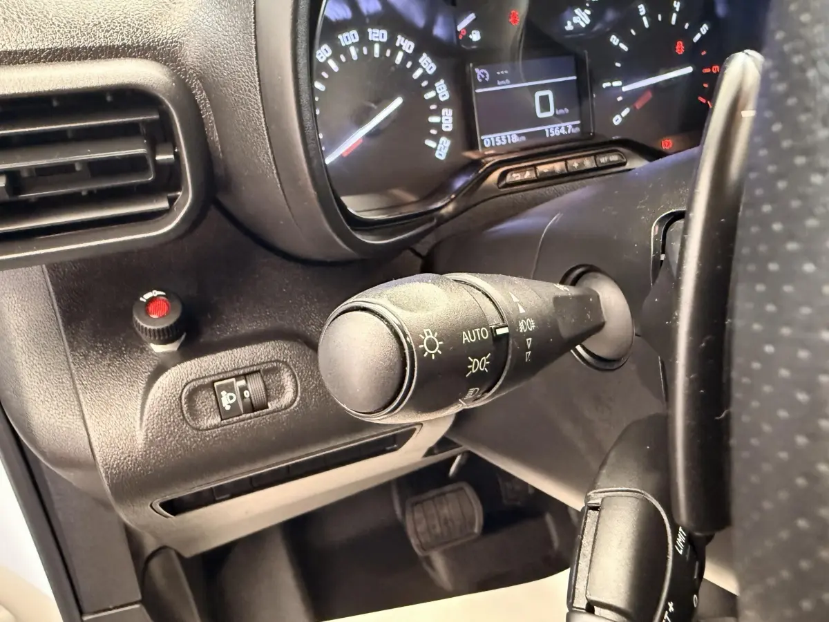 Gros plan sur la commande des phares et le tableau de bord du Citroën Berlingo blanc, vue côté conducteur.