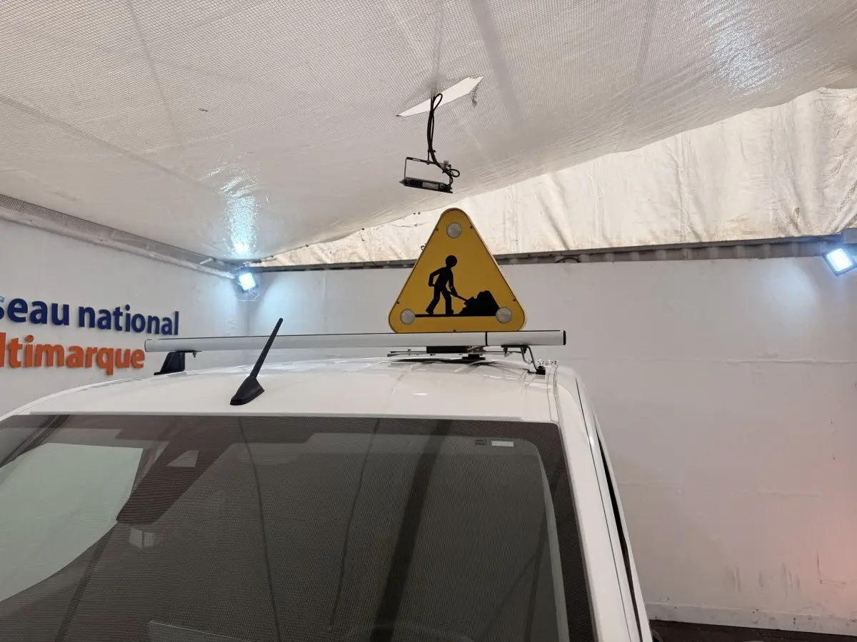 Vue avant rapprochée du toit blanc d’un Citroën Berlingo avec panneau triangulaire de chantier fixé dessus.