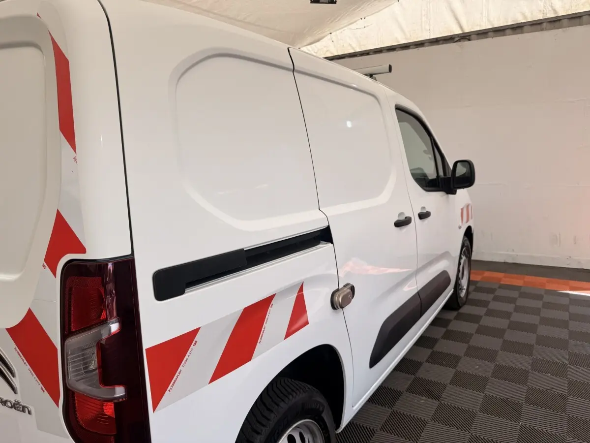 Vue 3/4 arrière droite d’un Citroën Berlingo blanc avec bandes rouges diagonales et porte latérale coulissante.
