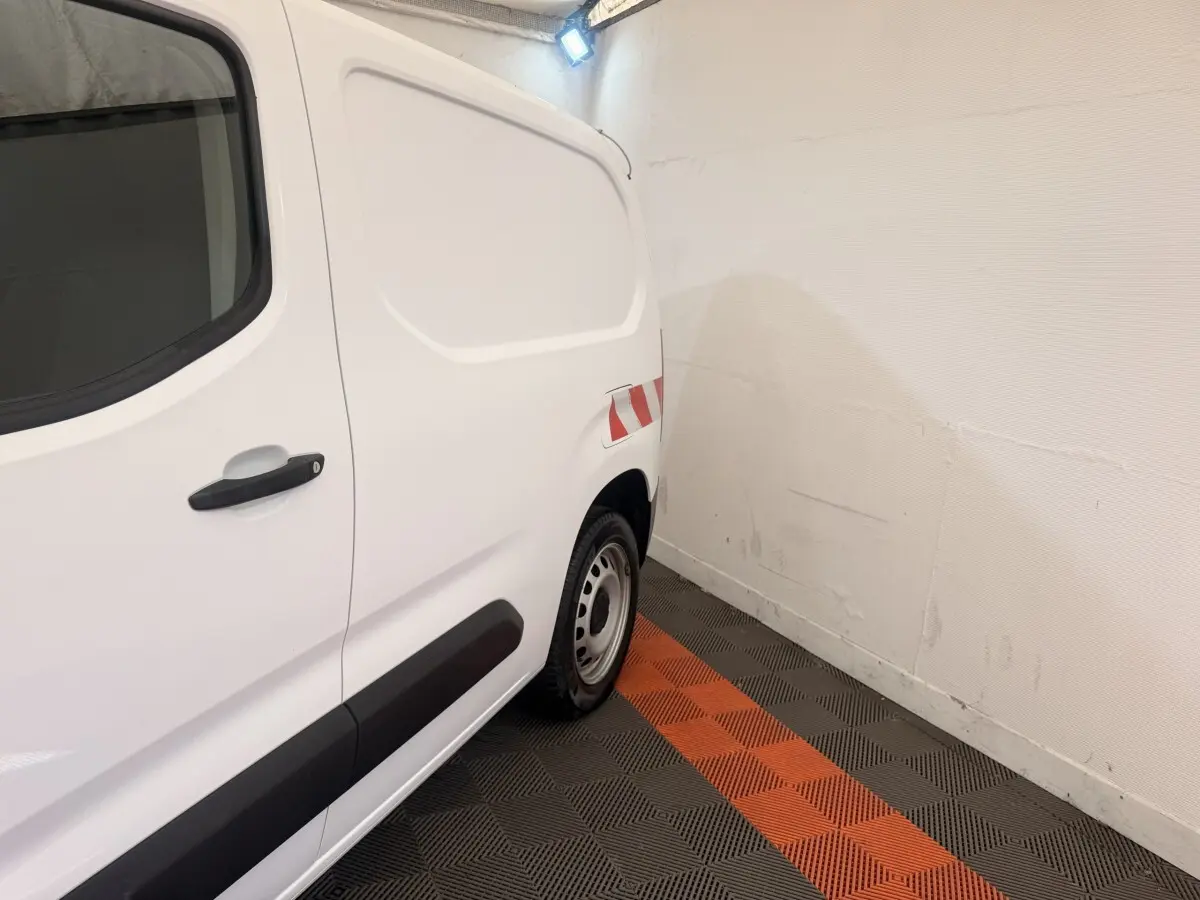 Vue latérale arrière droite d’un utilitaire Citroën Berlingo blanc avec marquage réfléchissant rouge et blanc.