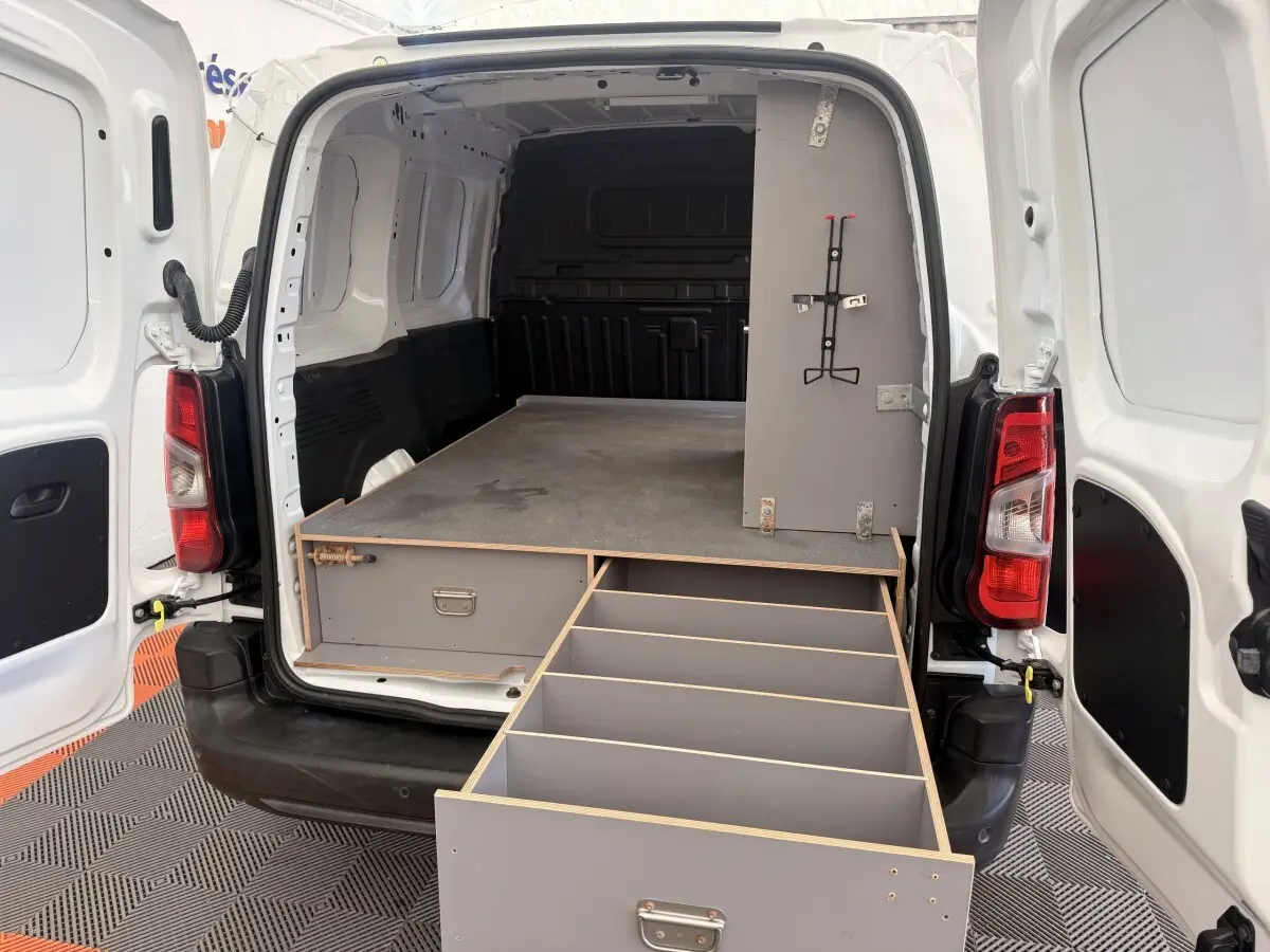 Vue arrière du Citroën Berlingo blanc avec portes ouvertes et tiroir de rangement gris déployé dans l’espace de chargement.