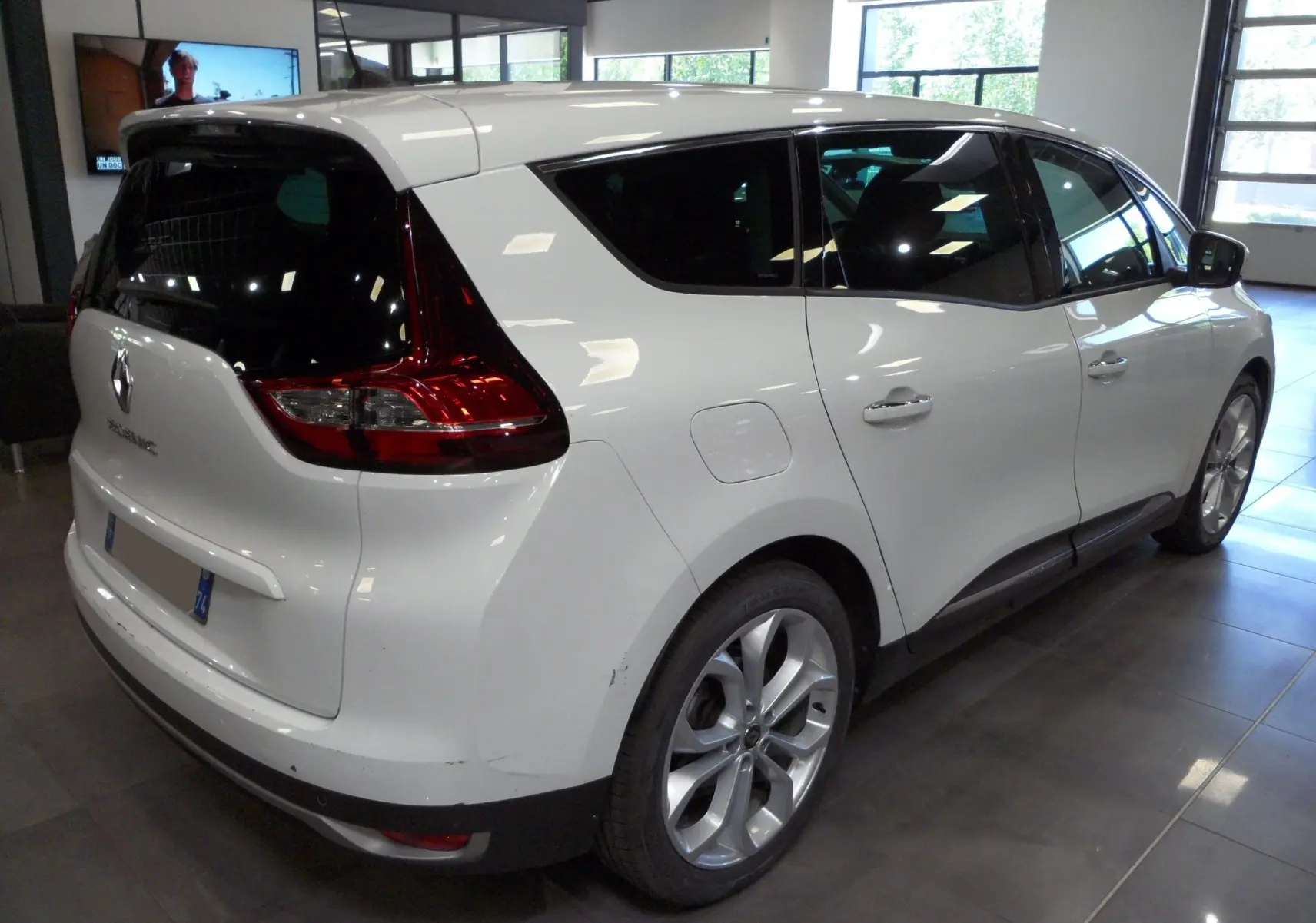 Vue 3/4 arrière droite d'un Renault Grand Scenic IV blanc Glacier en intérieur, avec vitres teintées et jantes alliage.