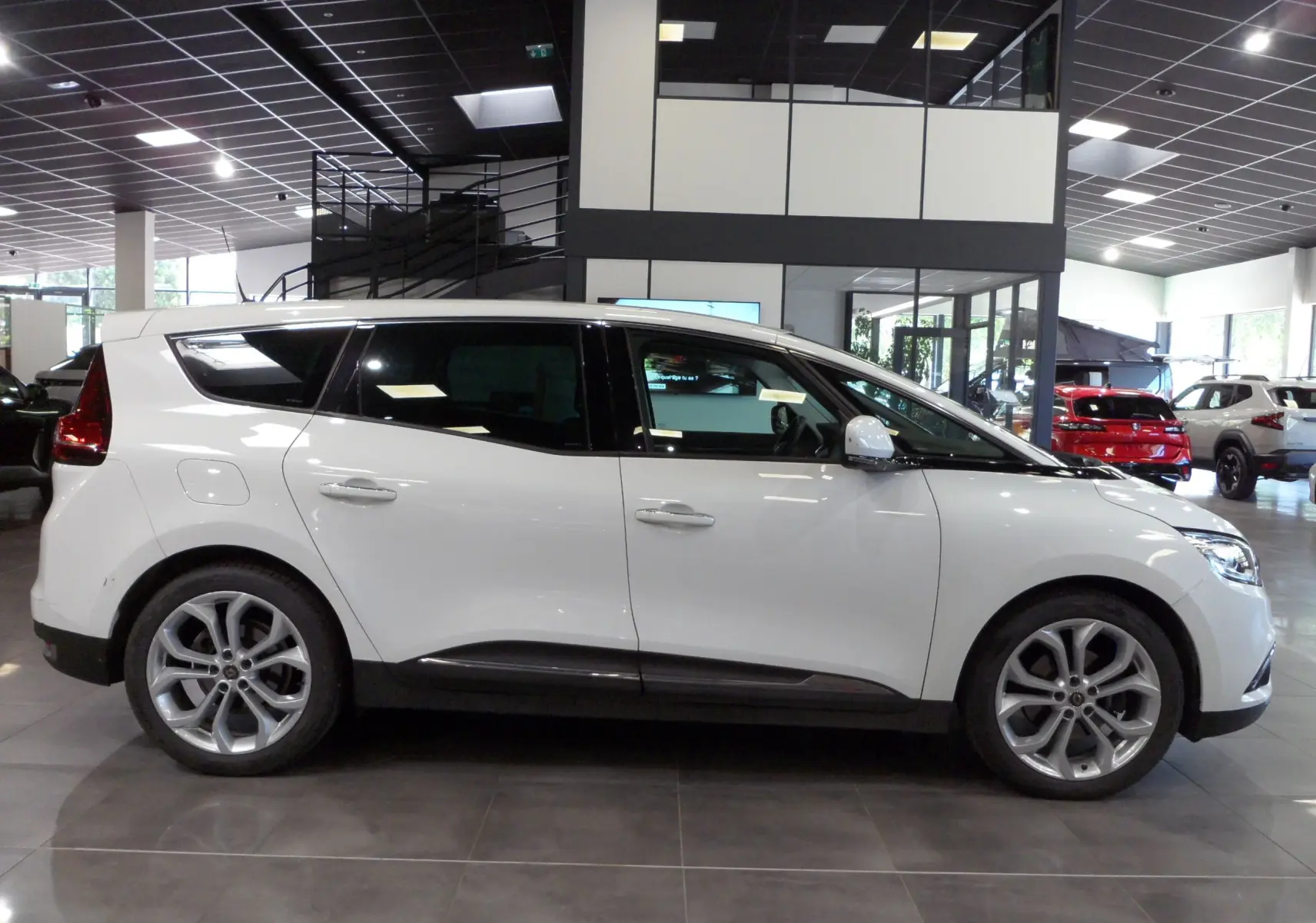 Profil droit d'un Renault Grand Scenic IV blanc Glacier en intérieur, soulignant ses lignes fluides et ses jantes alliage.