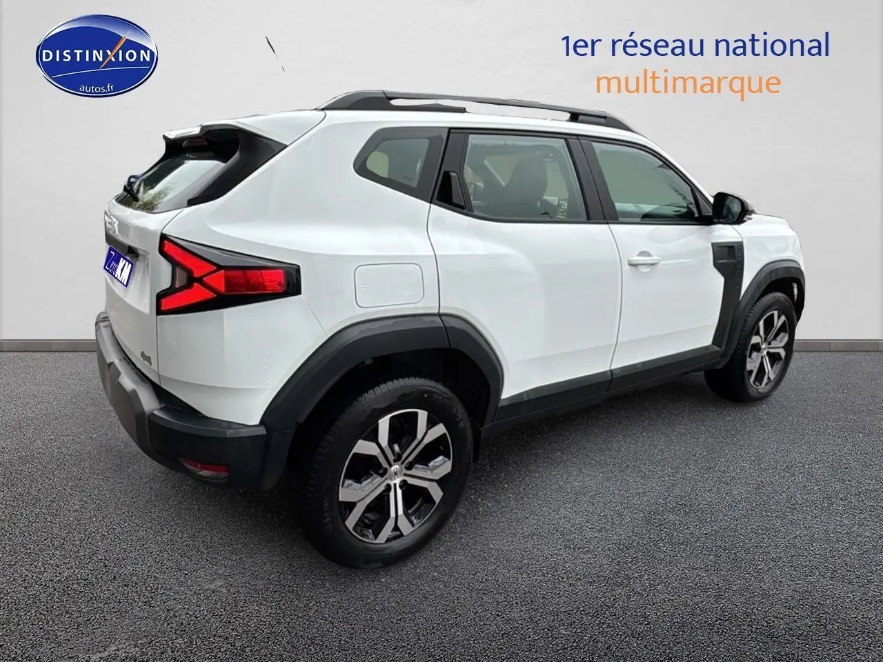 Vue 3/4 arrière droite d'un Dacia Duster blanc arctic 2025 avec barres de toit et feux arrière LED distinctifs.