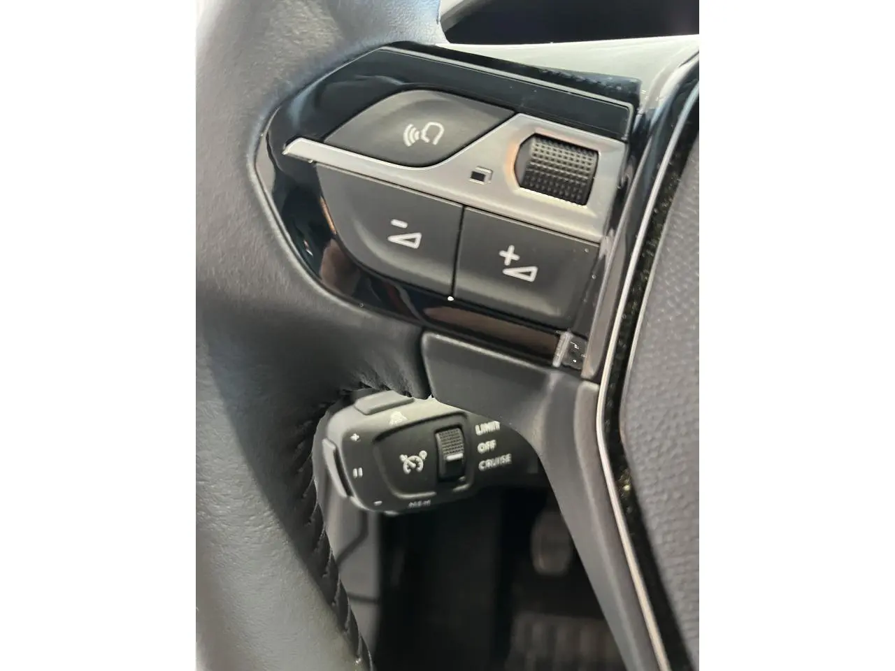 Gros plan sur commandes de régulateur de vitesse et volume au volant cuir noir de la Peugeot 208 gris clair Selenium