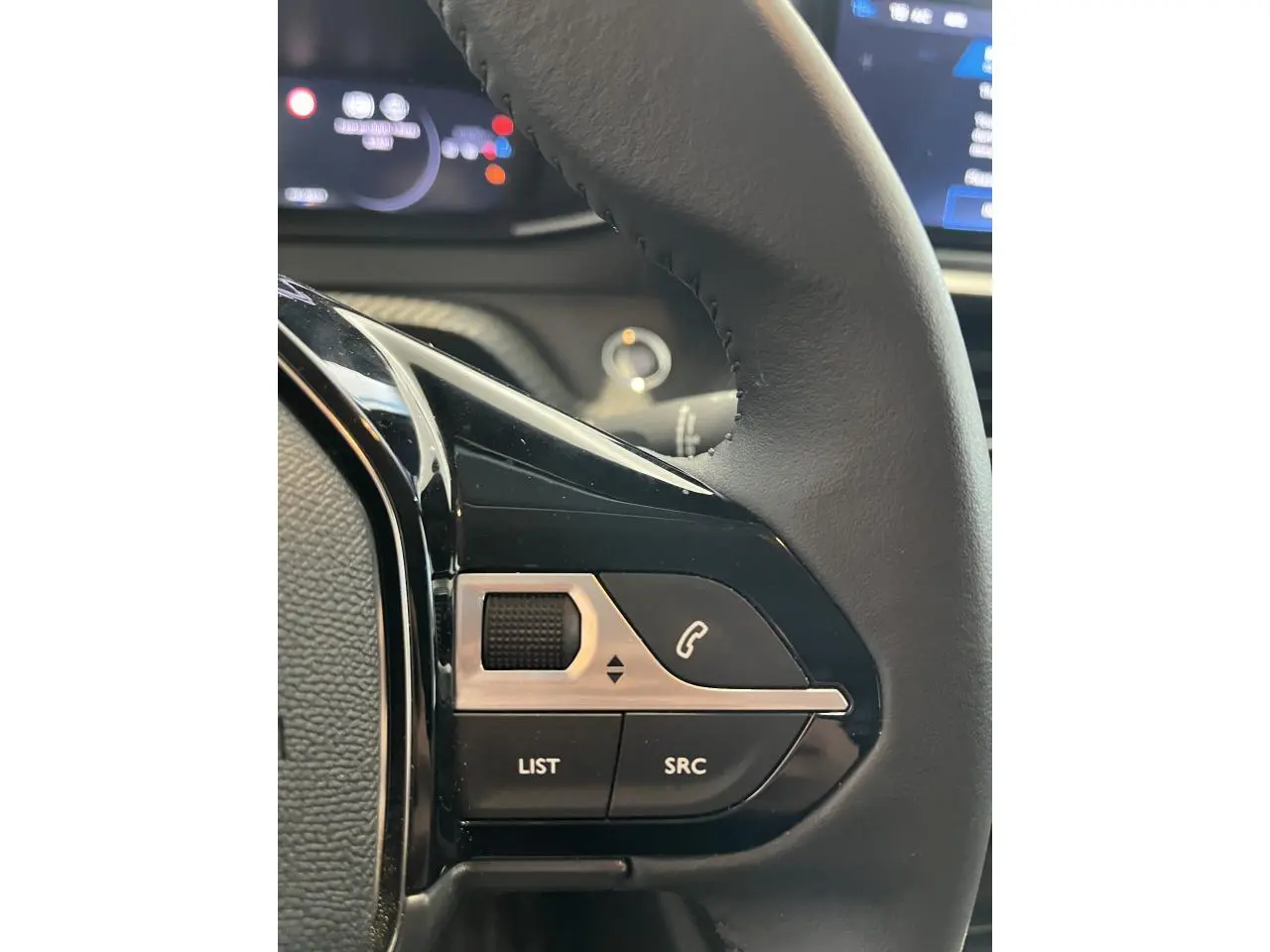 Gros plan sur les commandes multimédia noires et argentées du volant cuir de la Peugeot 208 gris clair Selenium.