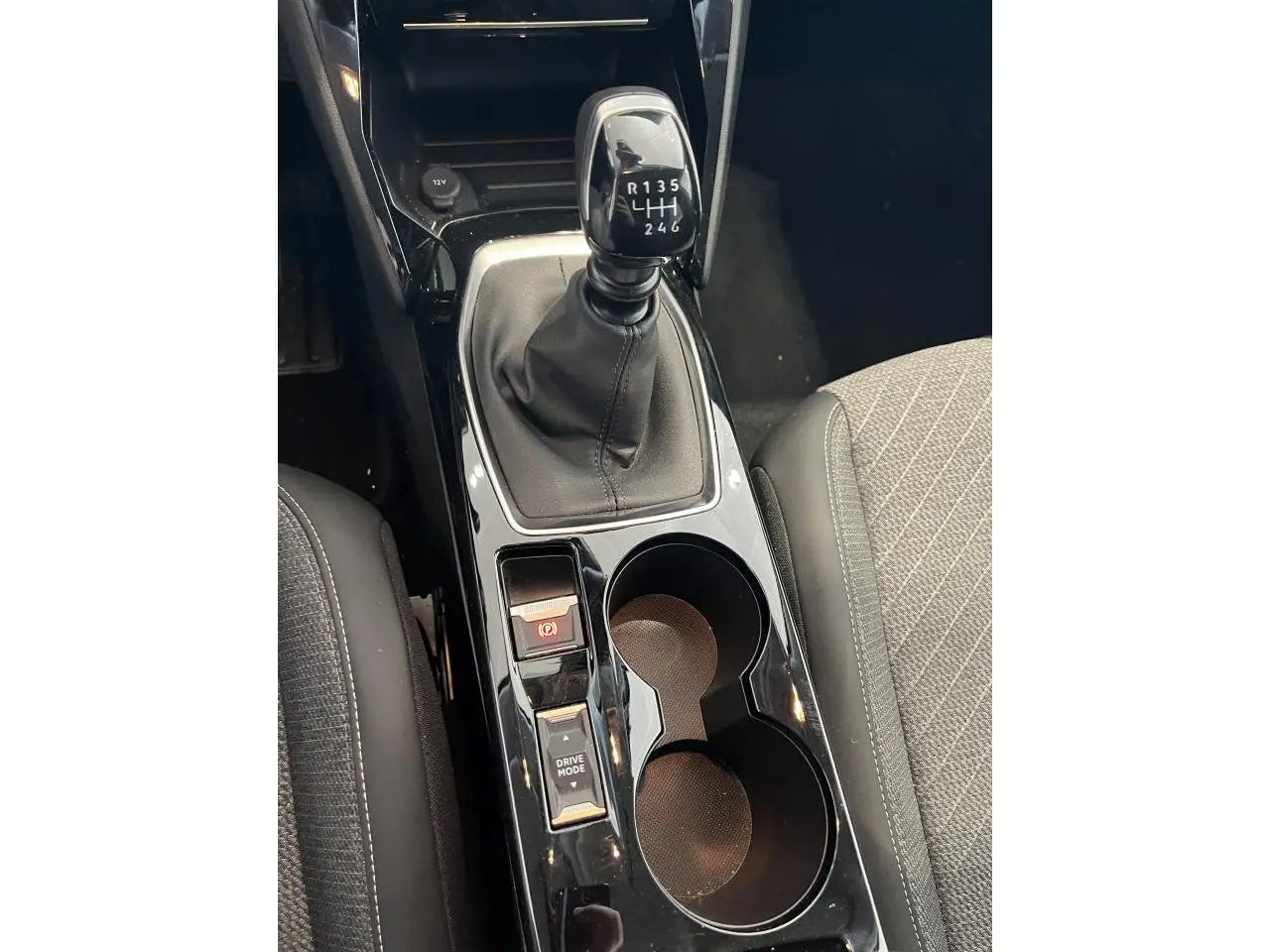 Vue rapprochée de la console centrale noire brillante avec levier de vitesse manuelle et porte-gobelets dans une Peugeot 208 gris clair.