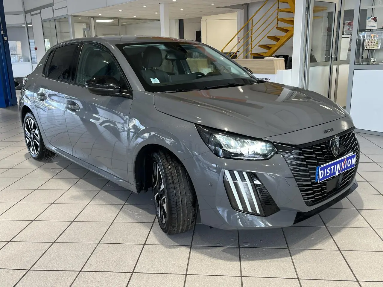 Peugeot 208 gris clair selenium vue 3/4 avant droit en showroom avec calandre noire et feux LED griffés.