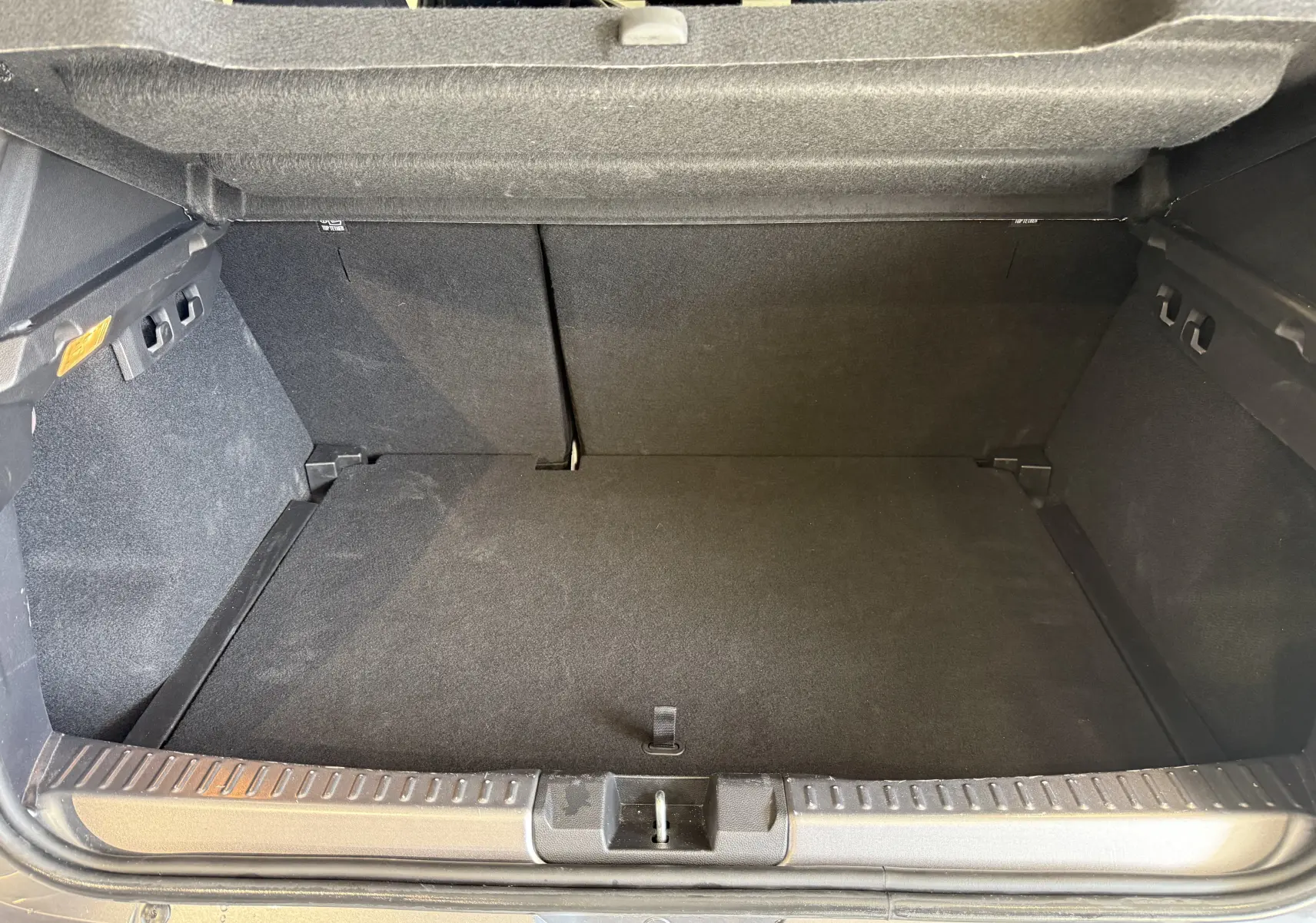Coffre ouvert vu de l'arrière d'une Dacia Sandero gris 2025, intérieur noir et espace de chargement vide.