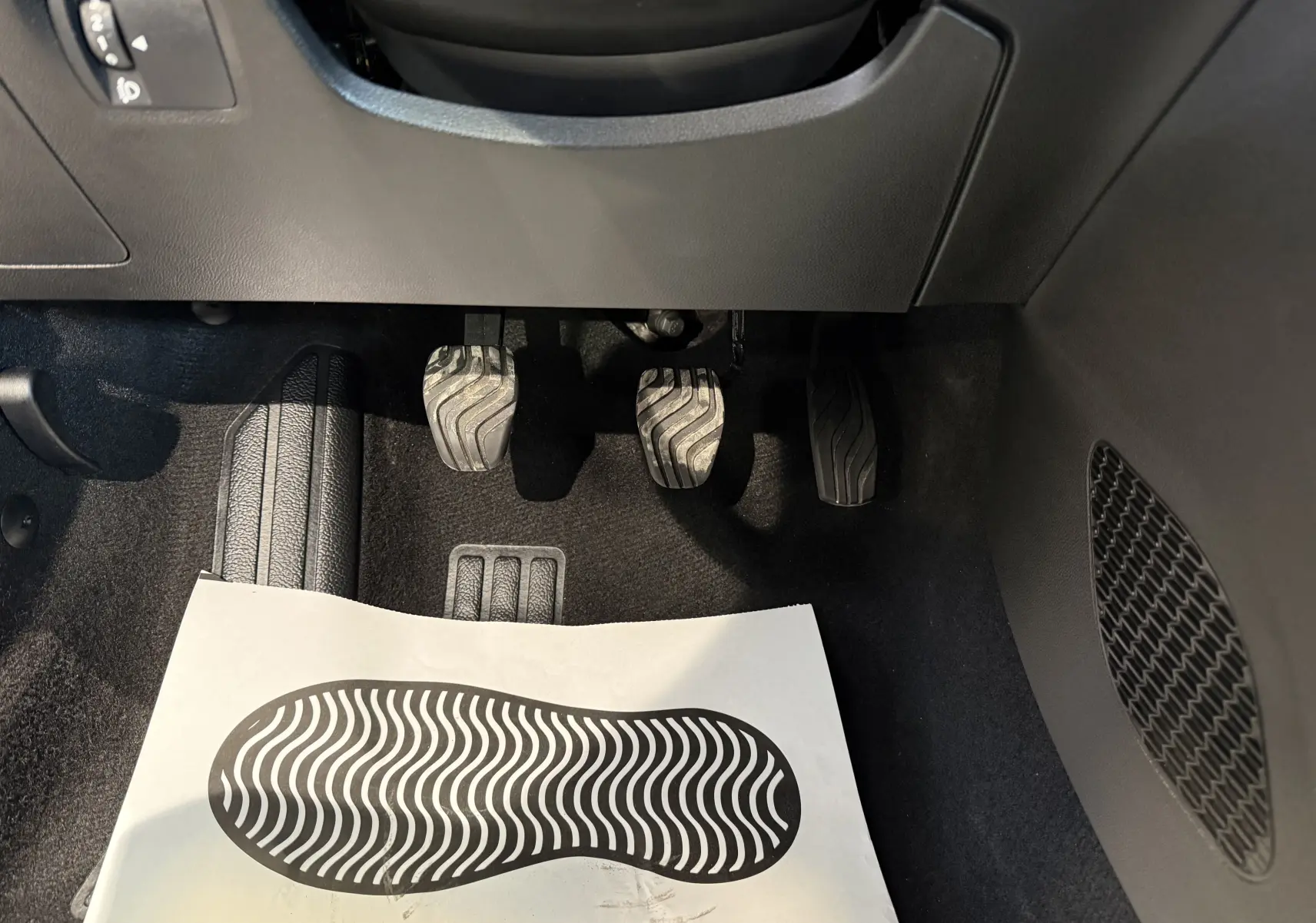 Vue rapprochée des pédales d’embrayage, frein et accélérateur d’une Dacia Sandero gris 2025 avec boîte manuelle.