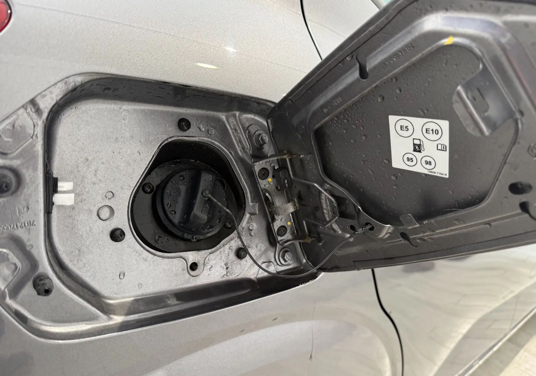 Gros plan sur la trappe à carburant ouverte côté gauche d’une Dacia Sandero gris 2025, avec bouchon essence visible.