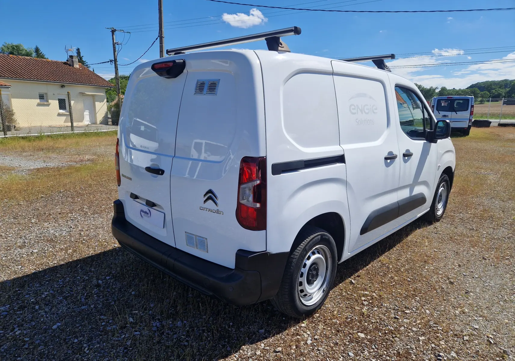 Vue 3/4 arrière droite d’un Citroën Berlingo blanc utilitaire 2020 avec barres de toit et marquage ENGIE Solutions sur la porte latérale.