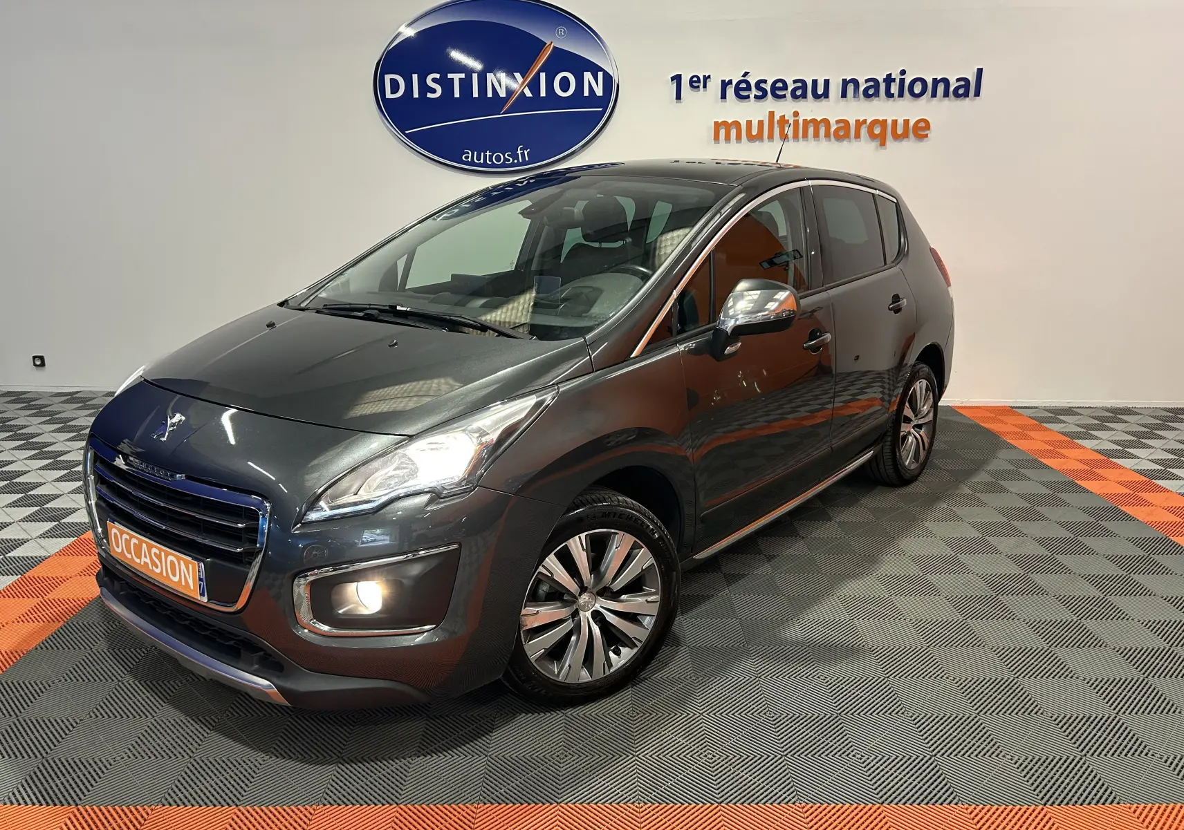 Peugeot 3008 gris en 3/4 avant droit, phare et antibrouillard allumés, avec jantes alliage et toit panoramique visible.