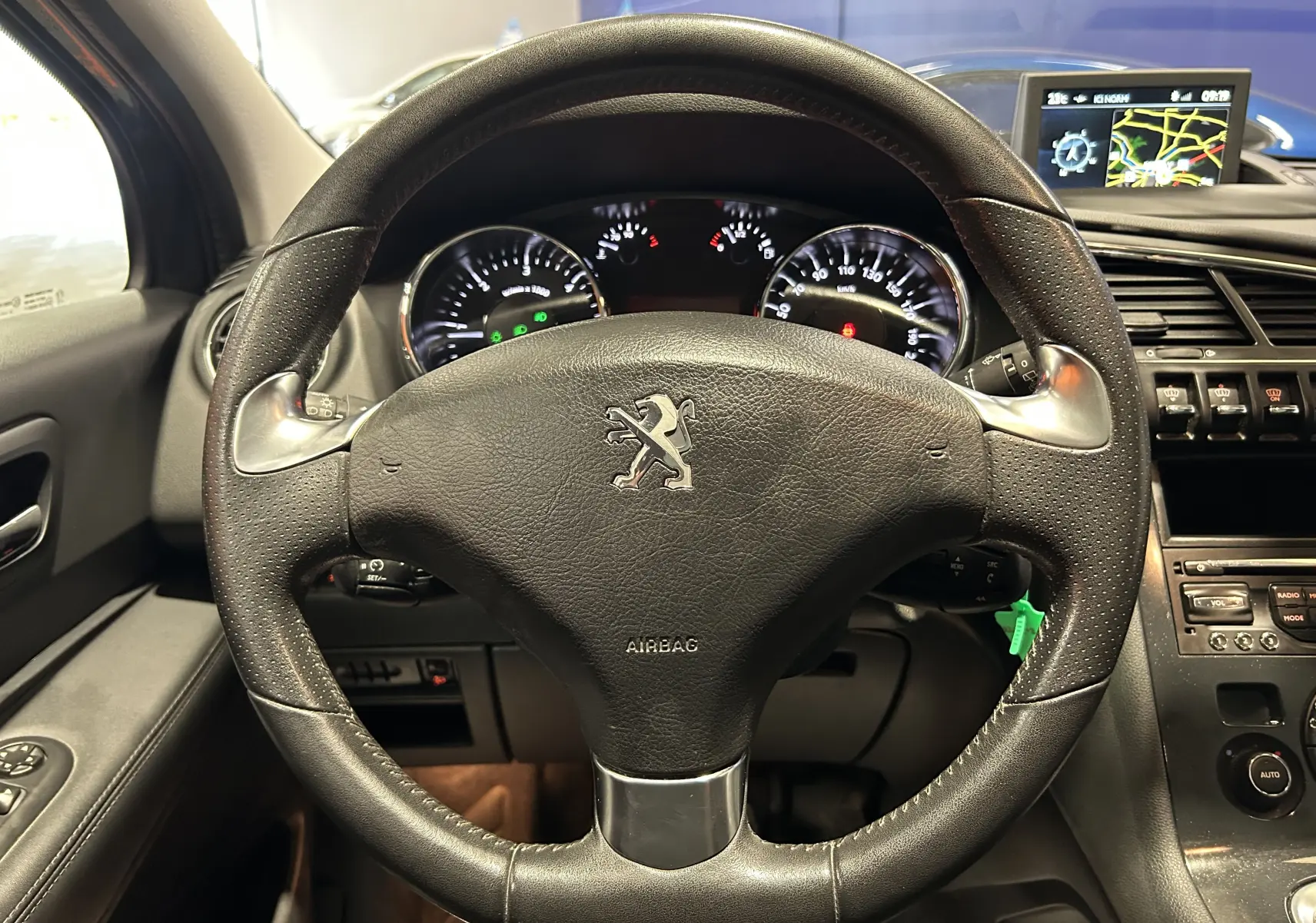 Vue rapprochée du volant en cuir noir du Peugeot 3008 gris, avec tableau de bord et écran GPS en arrière-plan.