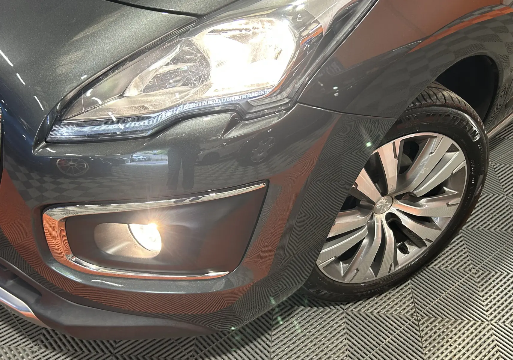 Gros plan sur l'avant droit gris métallisé du Peugeot 3008 avec phare et antibrouillard allumés, jante alliage visible.