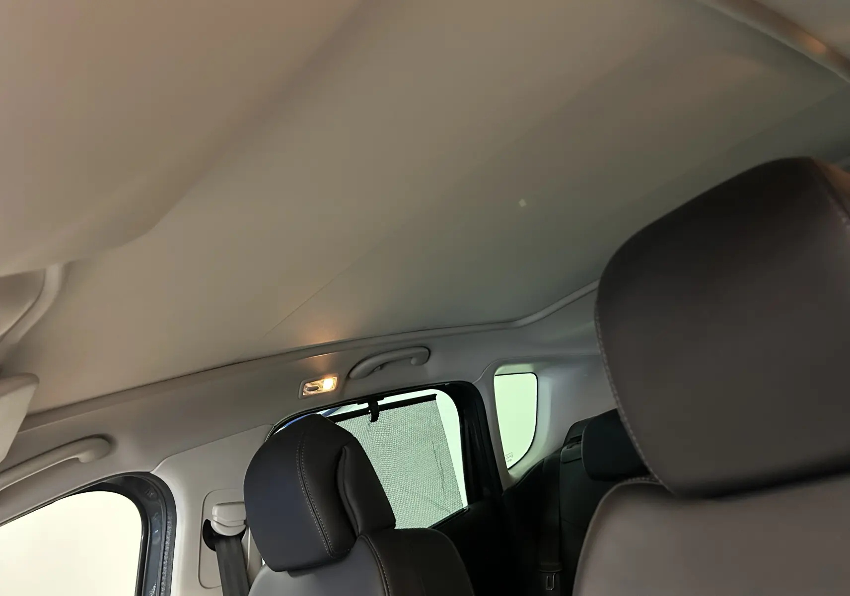 Vue intérieure arrière gauche du Peugeot 3008 gris, montrant les sièges en cuir et le toit panoramique avec store partiellement déployé.