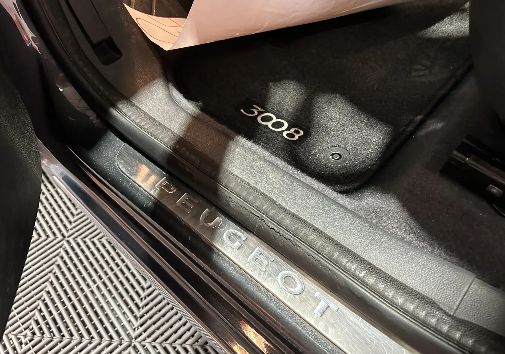 Gros plan sur le seuil de porte avec logo Peugeot et tapis noir marqué 3008, intérieur gris foncé visible.