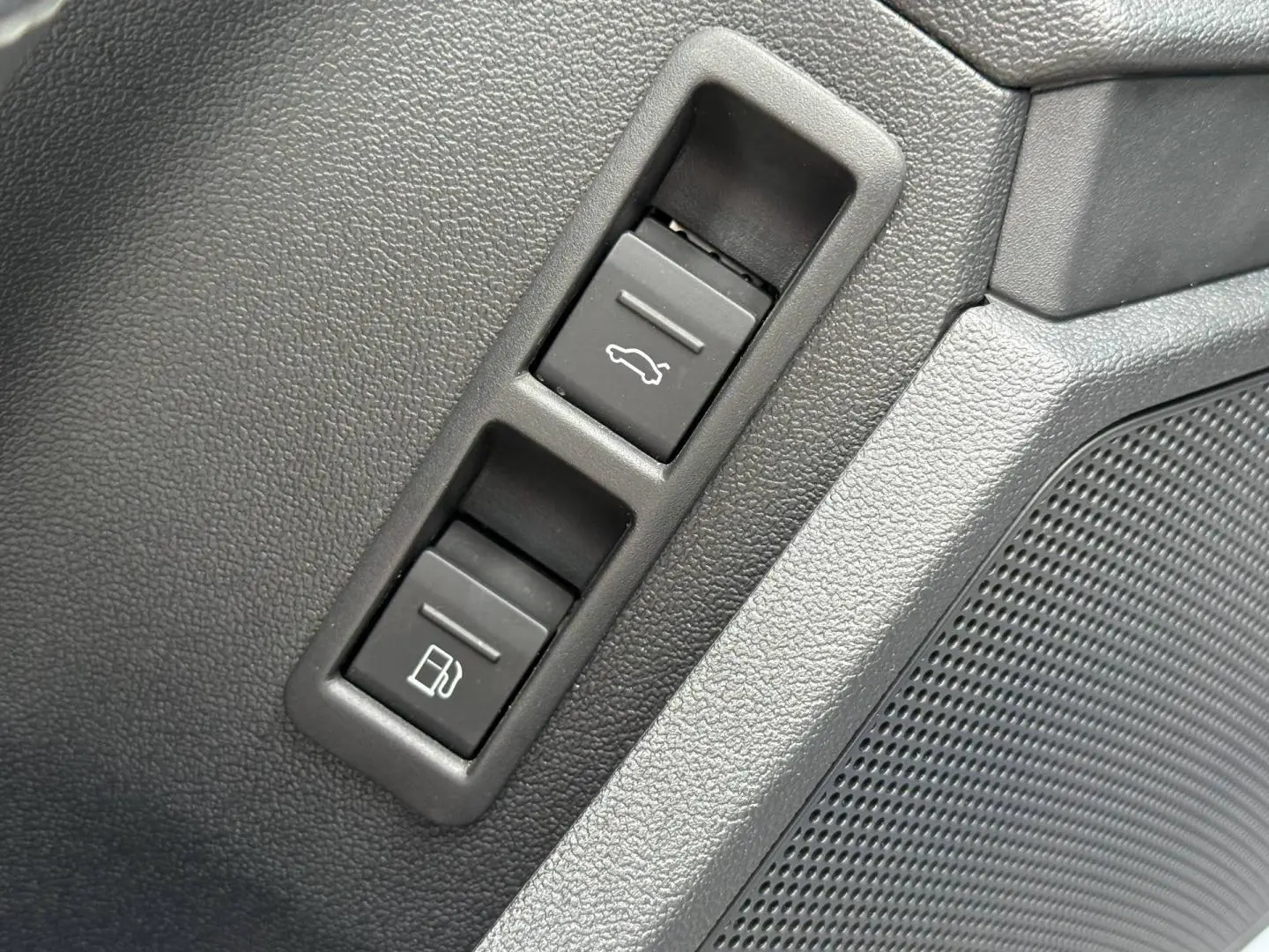 Détail intérieur montrant les boutons d'ouverture du coffre et de la trappe à carburant sur panneau noir texturé.