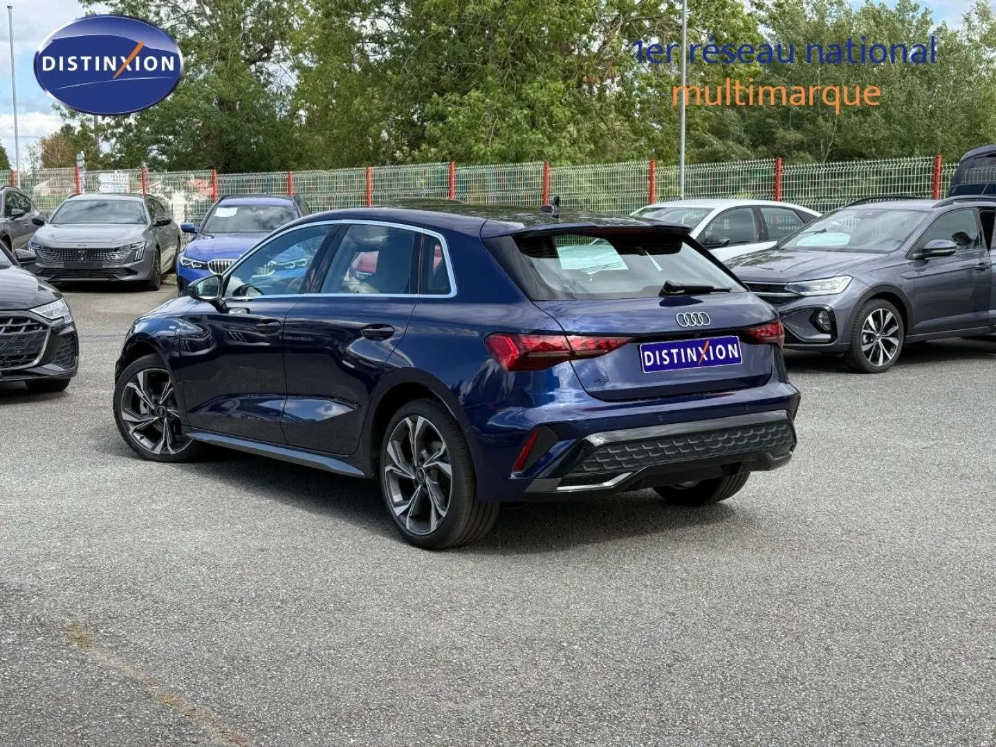 Audi A3 Sportback bleu Navarre métallisé vue 3/4 arrière droit sur parking avec jantes alu distinctives.