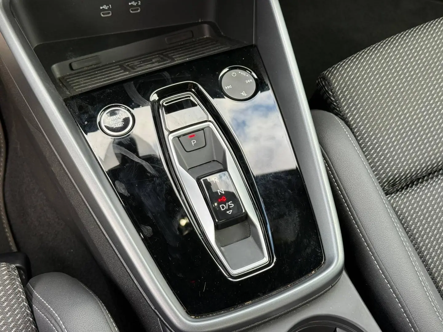 Gros plan sur la console centrale noire brillante avec sélecteur de boîte automatique et tissu gris du siège Audi A3 Sportback.