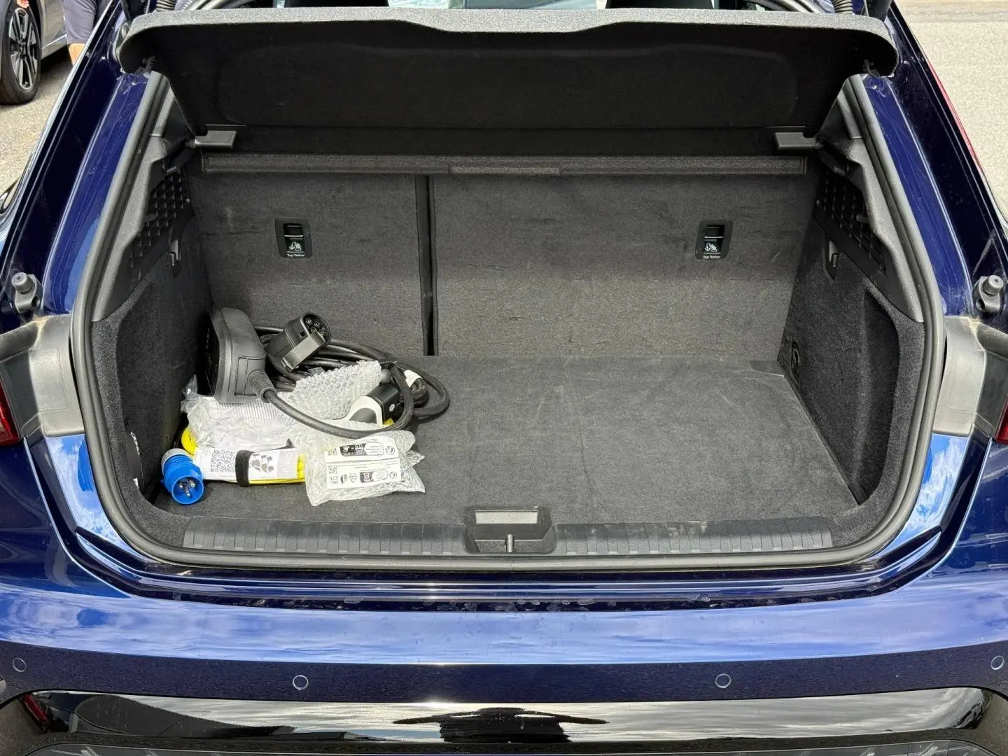Coffre ouvert vu de l'arrière d'une Audi A3 Sportback 2025 bleu Navarre métallisé avec câbles de recharge visibles.