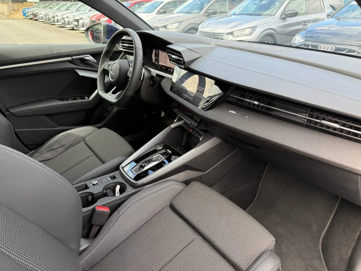 Vue intérieure côté conducteur de l'Audi A3 Sportback 2025, avec sièges tissu noir et tableau de bord moderne.