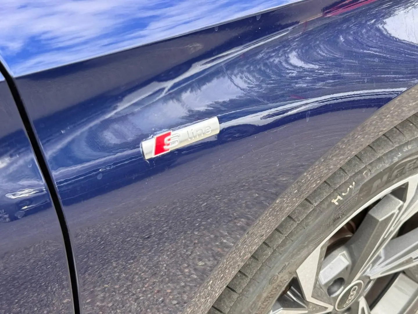 Gros plan sur l’aile avant droite bleu Navarre métallisé avec logo S line et jante alu Audi A3 Sportback 2025.