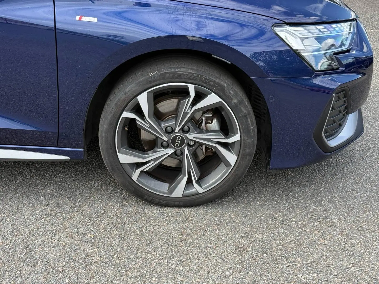 Gros plan sur la roue avant droite et partie avant bleue métallisée d'une Audi A3 Sportback S line 2025.