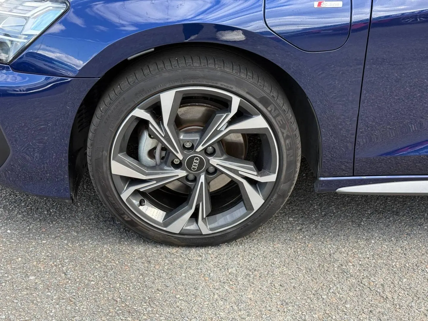 Gros plan sur la roue avant gauche d’Audi A3 Sportback Bleu Navarre métallisé avec jante alliage S line et logo Audi.
