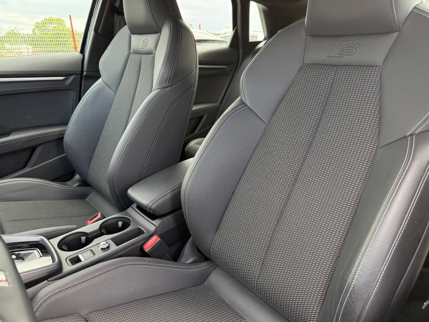 Gros plan sur les sièges avant sport noirs avec logo S embossé, accoudoir central et console d'une Audi A3 Sportback 2025.