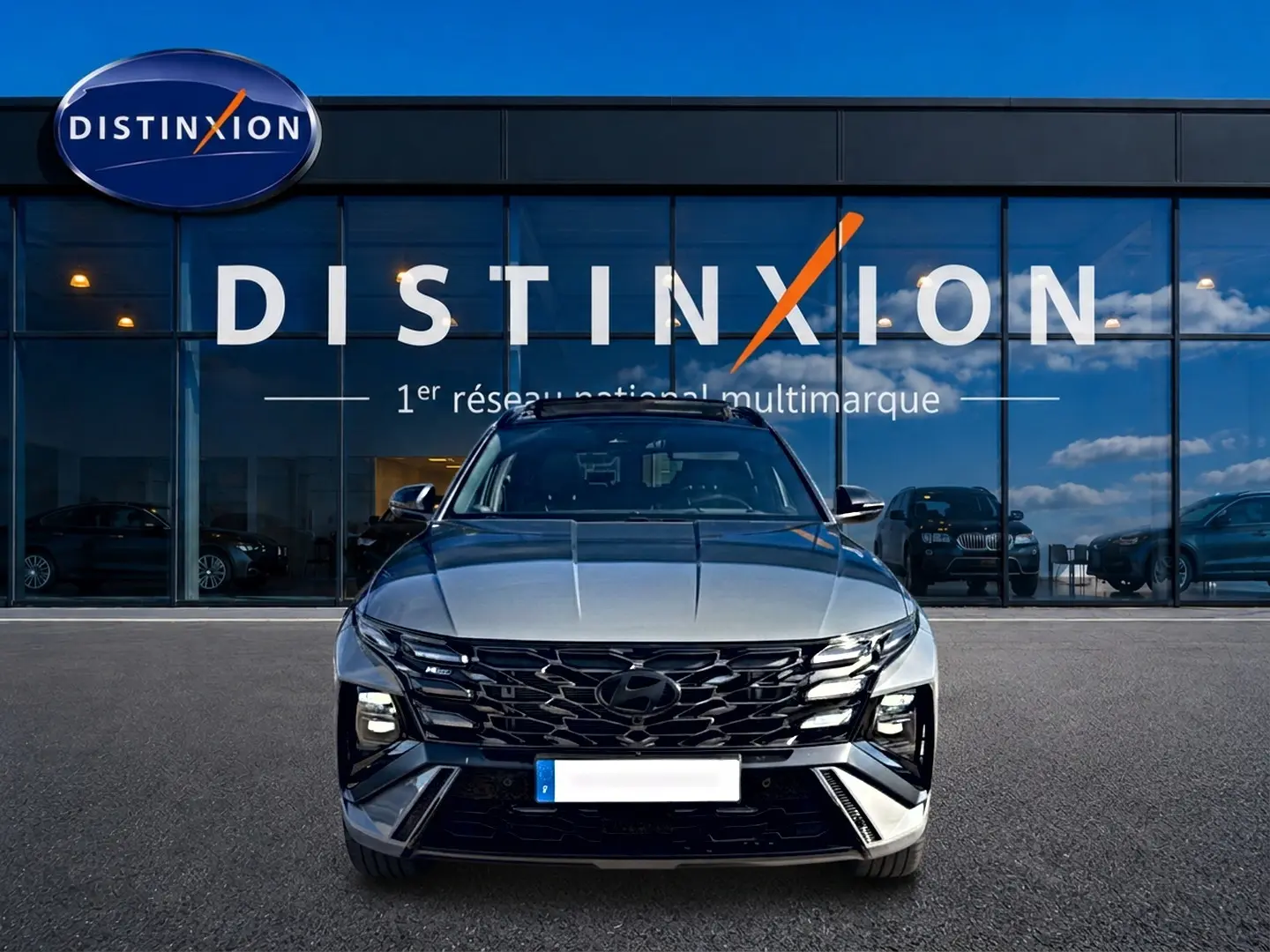 Vue frontale d'un Hyundai Tucson gris shadow 2026 avec calandre noire et phares LED devant un showroom Distinxion.