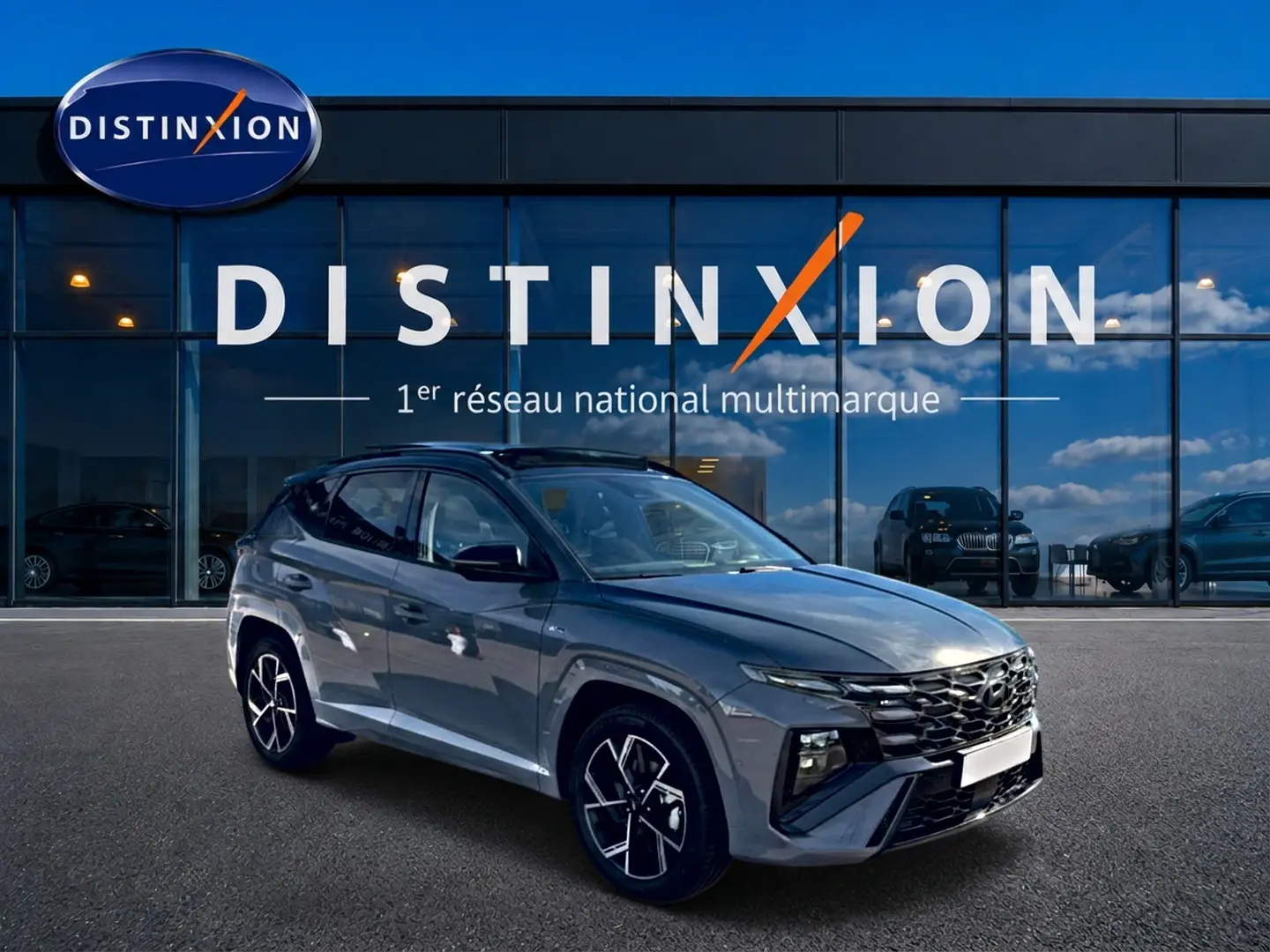 Hyundai Tucson gris shadow en 3/4 avant droit, avec calandre noire et jantes alu distinctives, devant vitrine Distinxion.
