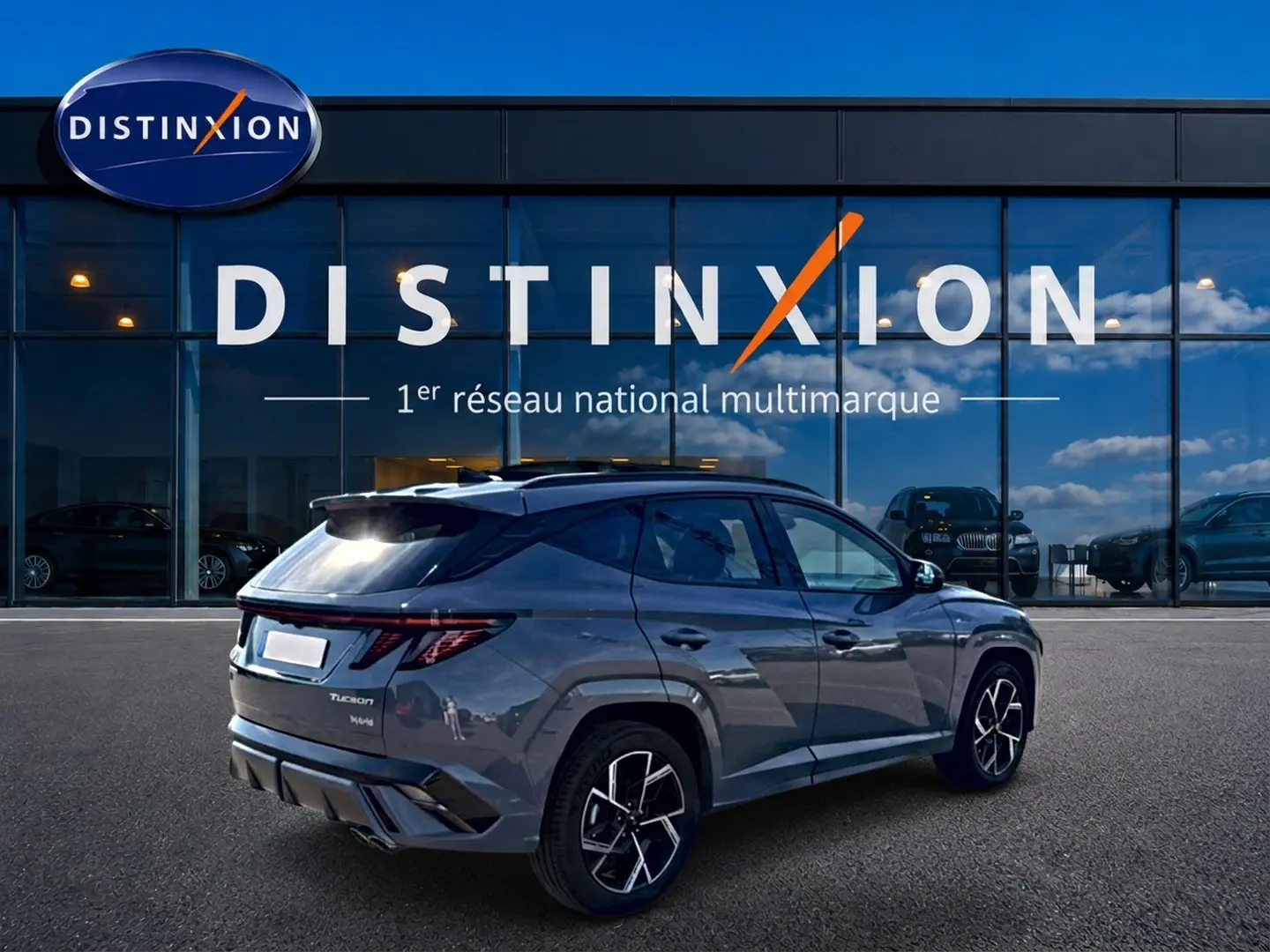 Vue 3/4 arrière droite d’un Hyundai Tucson gris shadow avec jantes alu et feux arrière LED, devant un showroom Distinxion.