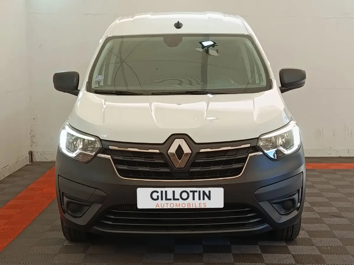 Vue frontale d’un Renault Express blanc avec phares allumés et pare-chocs noir mat dans un garage.