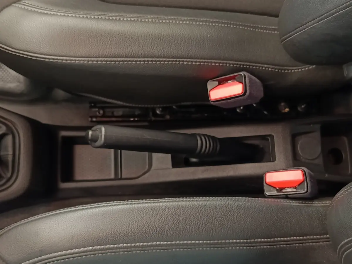 Vue rapprochée de la console centrale noire du Renault Express 2023, avec frein à main manuel et ceintures rouges.