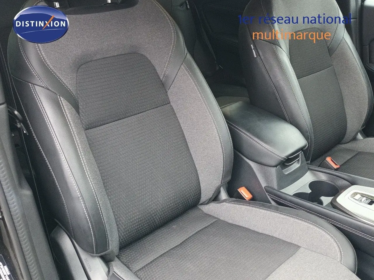 Gros plan sur les sièges avant en tissu et cuir noir du Nissan Qashqai e-POWER 2025, avec accoudoir central visible.