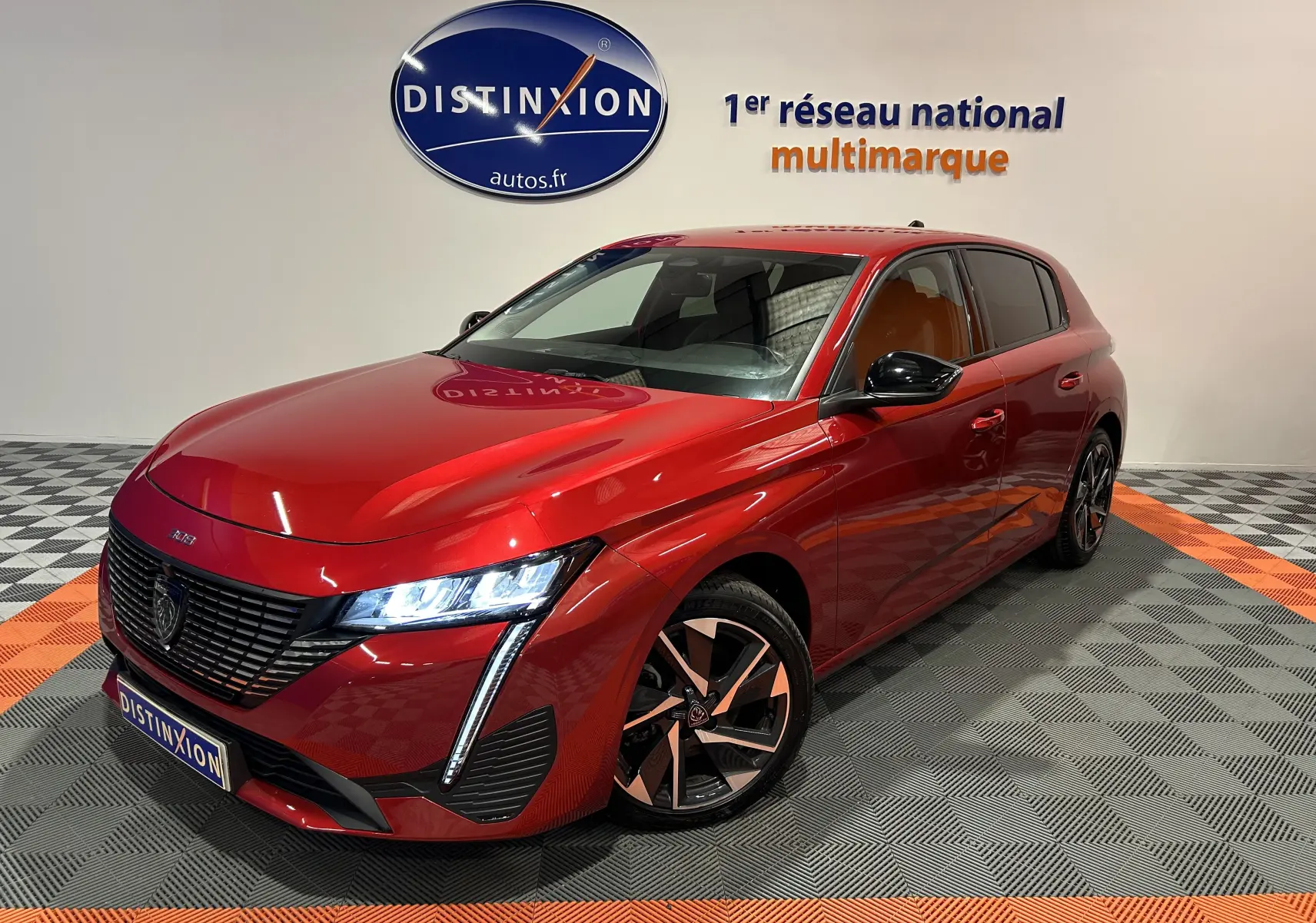 Peugeot 308 rouge vue 3/4 avant droit avec phares allumés et jantes alliage bicolores dans showroom.