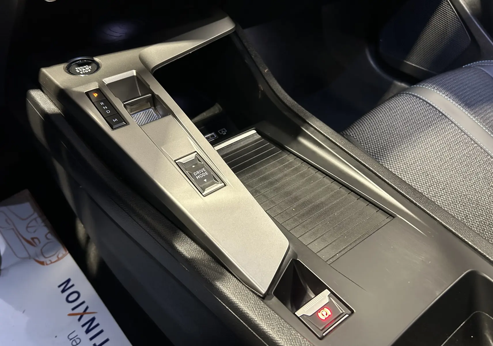 Vue rapprochée de la console centrale grise avec sélecteur de boîte auto et frein à main électrique dans Peugeot 308 rouge 2024.