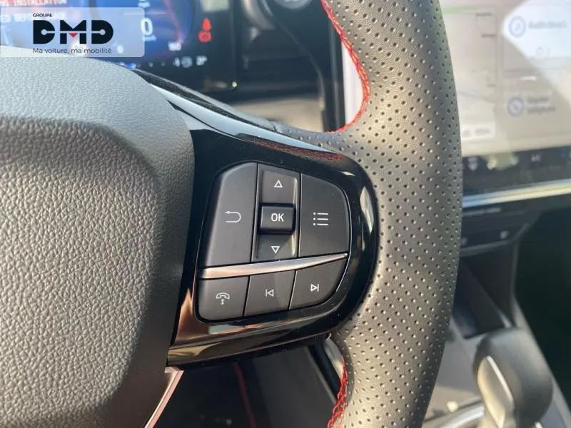 Gros plan sur les commandes multifonctions du volant perforé avec surpiqûres rouges d’un Ford Puma gris Cactus, intérieur moderne.