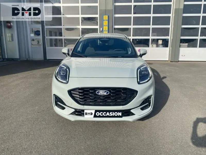 Vue avant d'une Ford Puma gris clair avec calandre noire et phares LED, stationnée devant un garage.