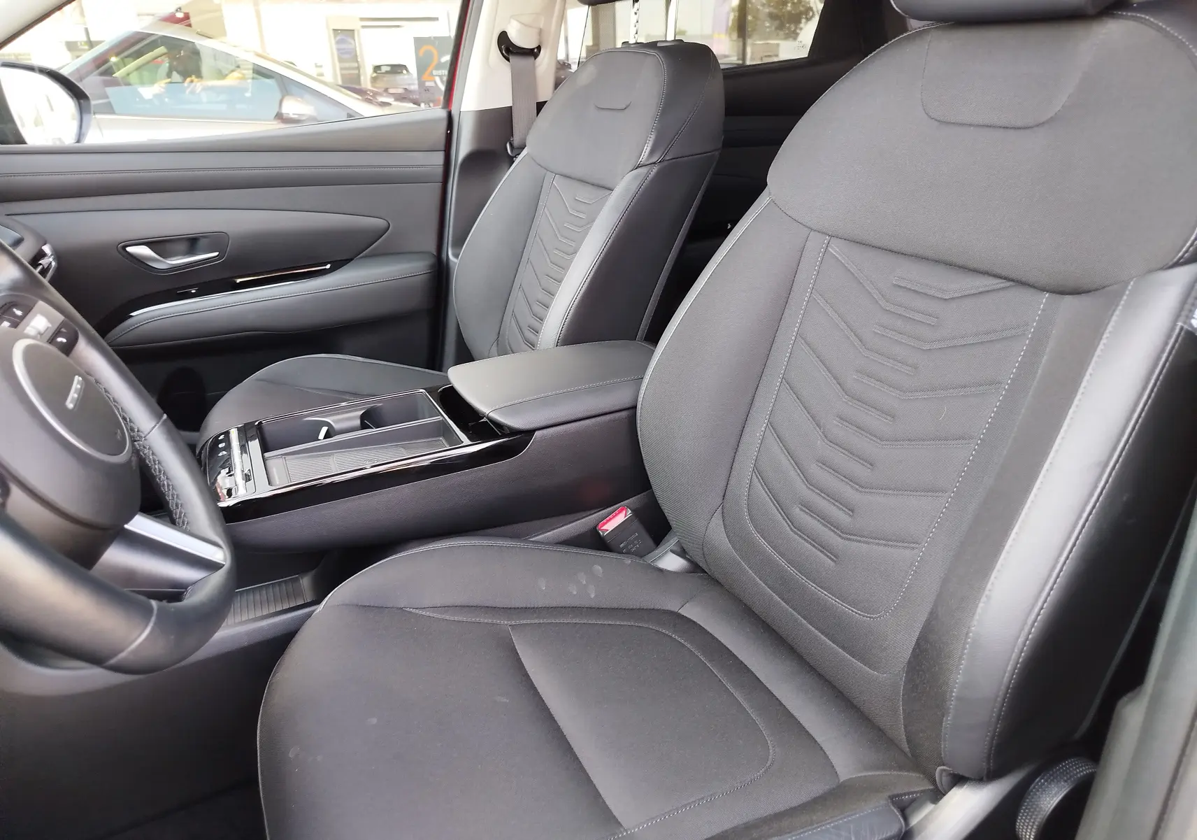 Vue intérieure du Hyundai Tucson 2024, sièges avant en tissu gris foncé avec console centrale et volant partiel visible.