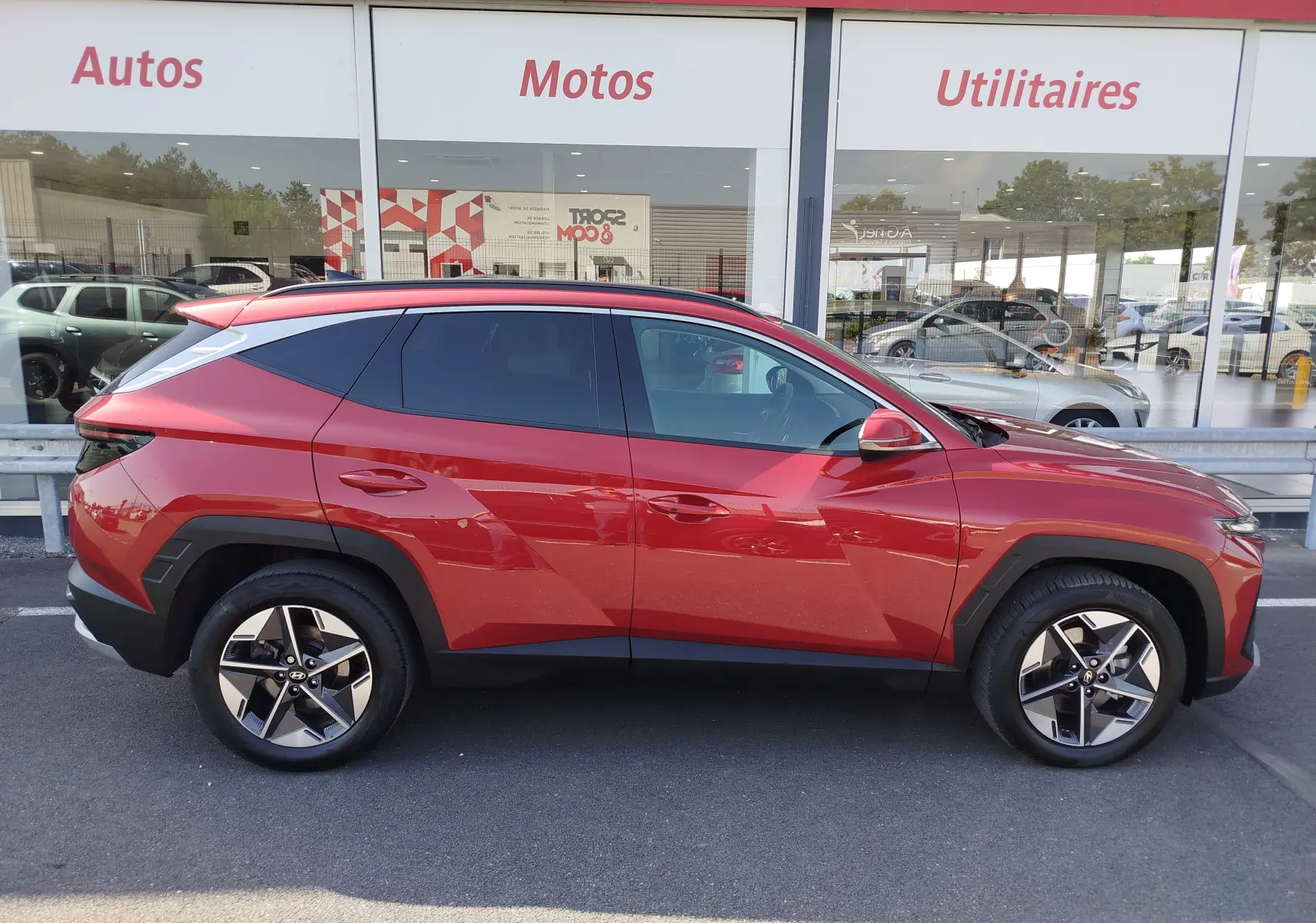 Vue de profil côté gauche d'un Hyundai Tucson 2024 rouge Ultimate Red Métal avec jantes bi-ton et vitres teintées.