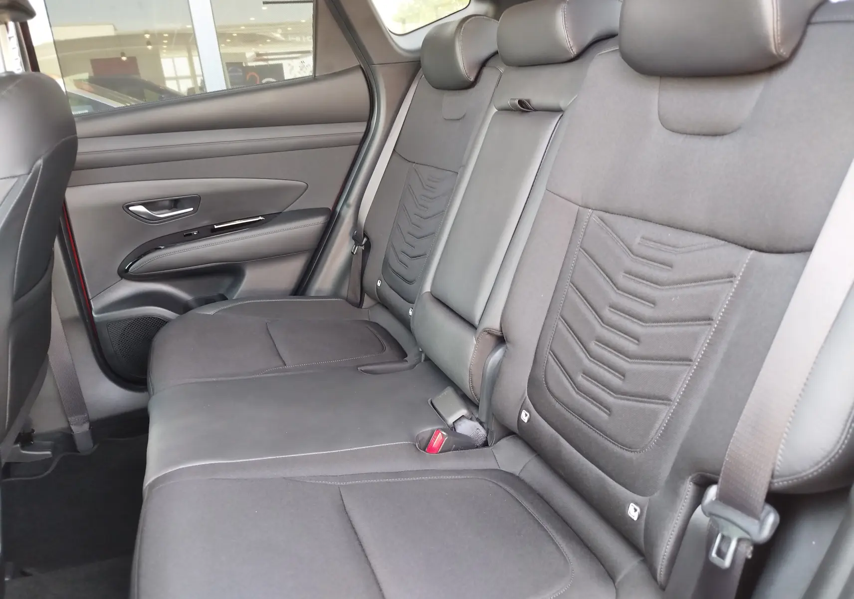 Vue intérieure côté droit des sièges arrière gris foncé du Hyundai Tucson 2024, avec appuie-têtes et ceintures visibles.