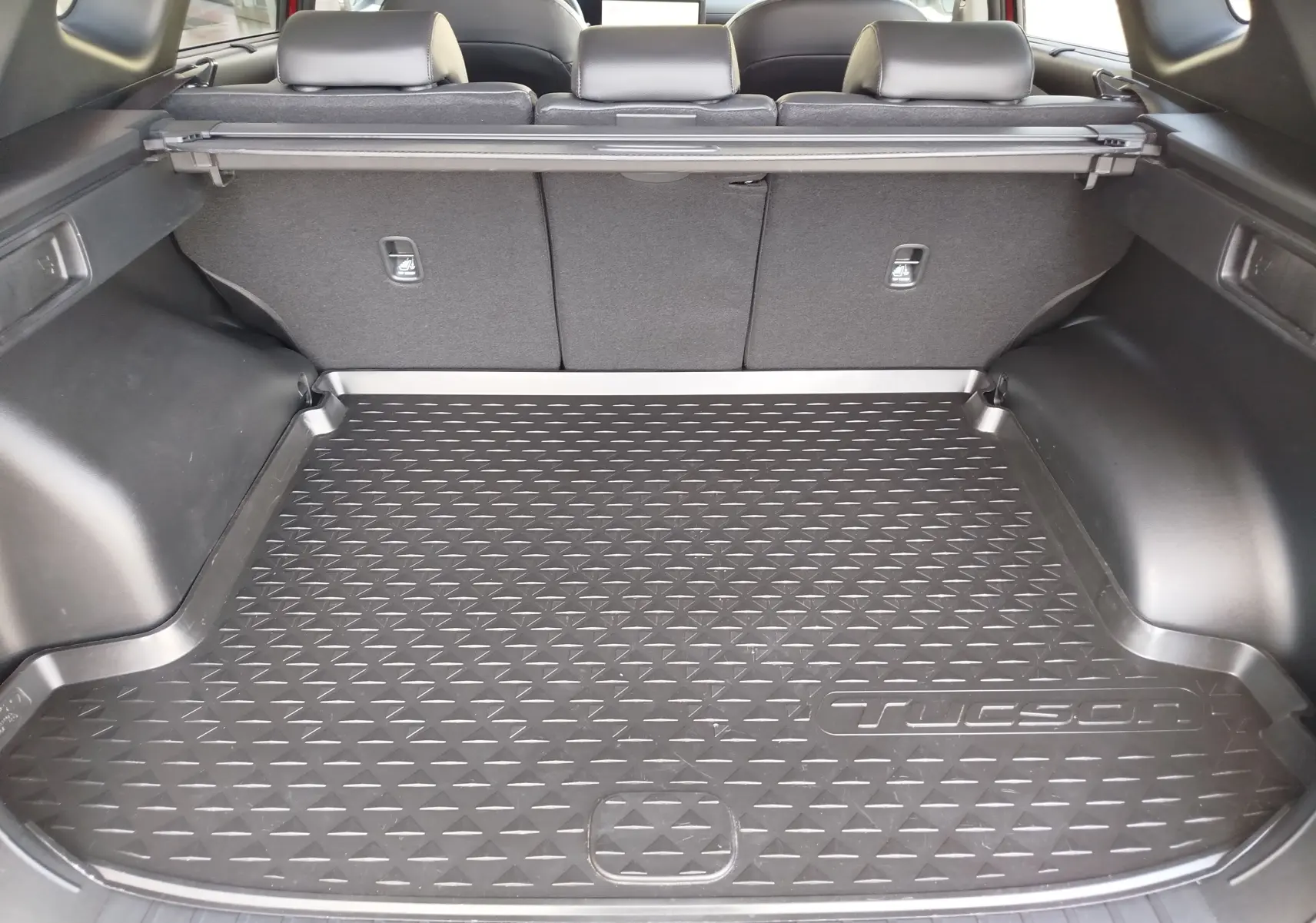 Vue intérieure du coffre du Hyundai Tucson 2024, avec tapis de protection noir marqué Tucson, sièges arrière rabattables visibles.
