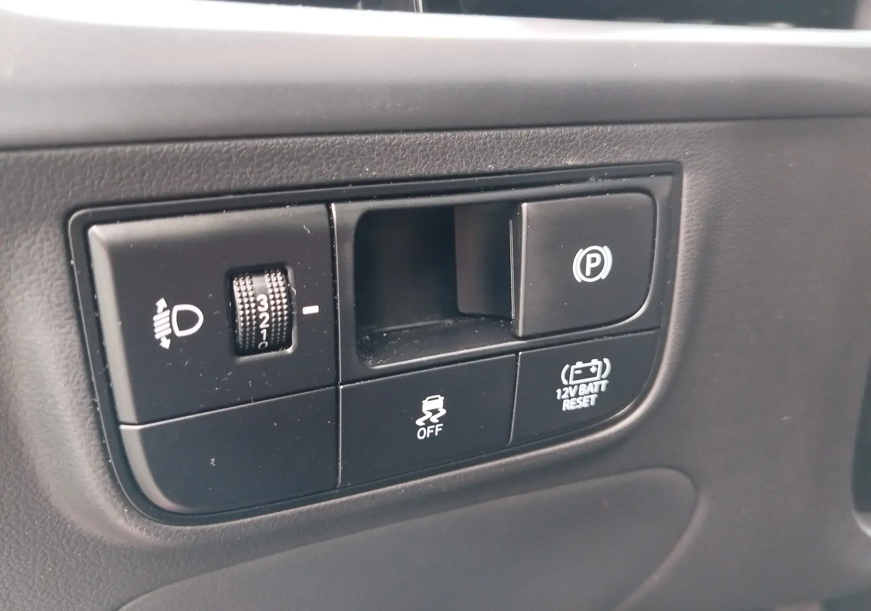 Gros plan sur les commandes intérieures noires du Hyundai Tucson 2024, avec réglage phares et frein de parking électrique.