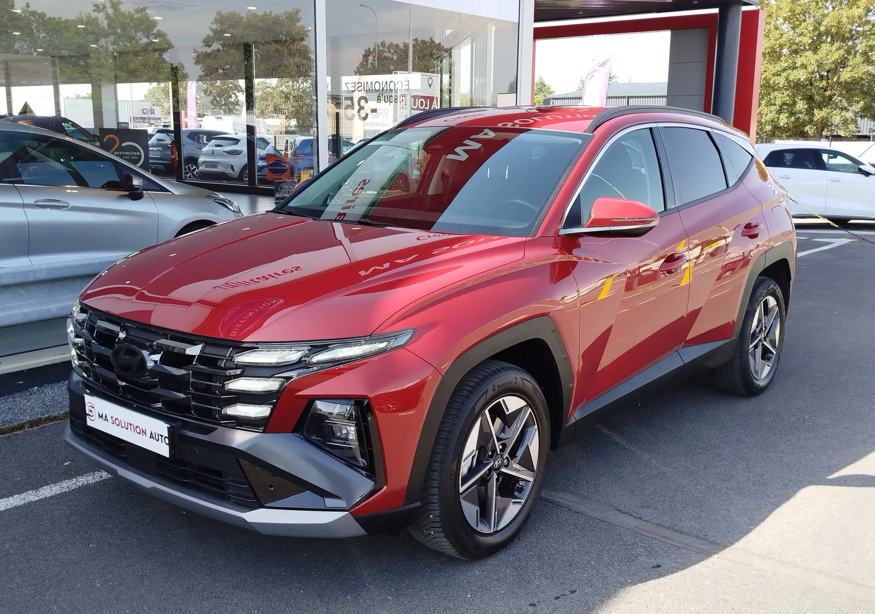 Hyundai Tucson 2024 rouge Ultimate Red Métal en 3/4 avant droit, avec calandre distinctive et jantes bi-ton.