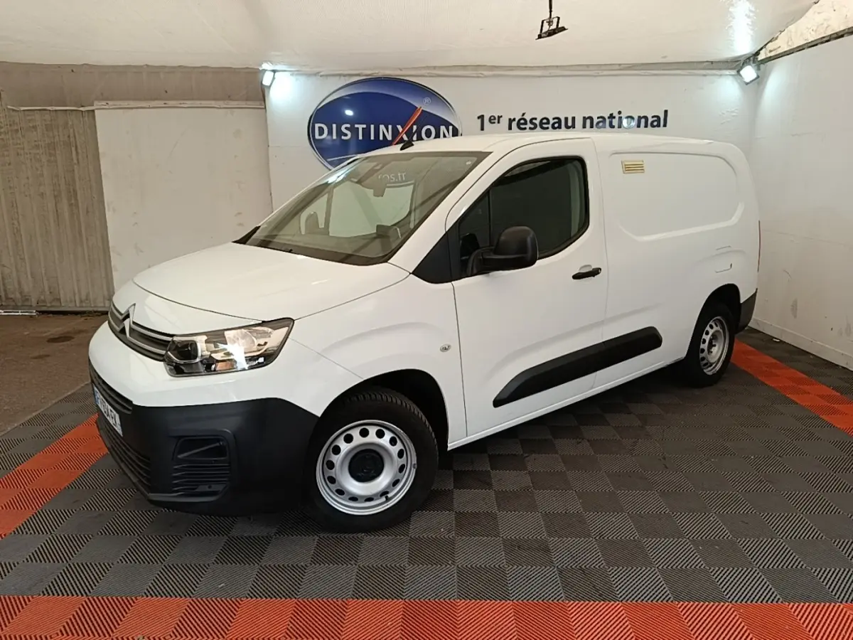 Vue 3/4 avant droite d’un utilitaire Citroën Berlingo XL blanc avec pare-chocs noirs et jantes acier en intérieur showroom.