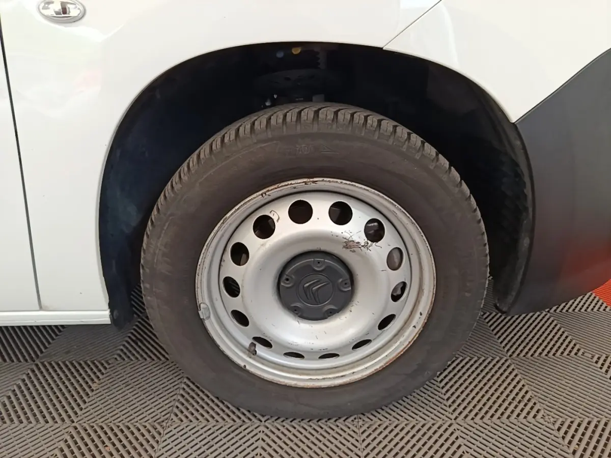 Gros plan sur la roue avant gauche en jante acier du Citroën Berlingo XL blanc, avec carrosserie visible en arrière-plan.